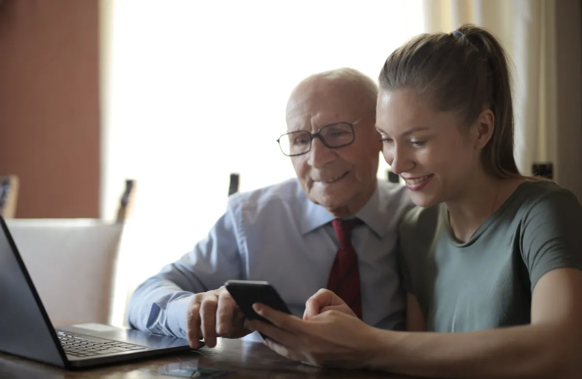 Um senhor e uma jovem sorrindo, olhando juntos o celular